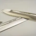 Two knives are laying on a table with one knife in the other.