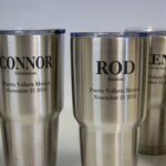 A group of four stainless steel cups with names and dates on them.
