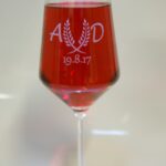 A red wine glass with the date and initials engraved on it.