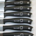 A row of knives with black handles and white lettering.