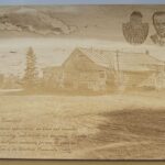 A wooden plaque with an image of two people and a barn.
