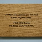 A wooden plaque with the words " neither the summit nor the trail know why we came."